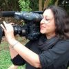 Woman with dark hair filming with a handheld video camera outdoors.