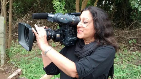 Woman with dark hair filming with a handheld video camera outdoors.
