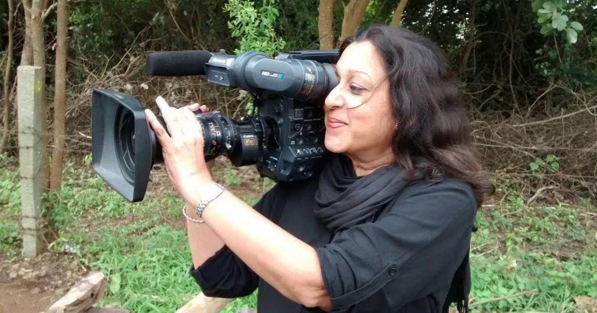 Woman with dark hair filming with a handheld video camera outdoors.