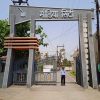 Entrance gate with tall grey pillars and a sign in Hindi reading 'Media City'; a security guard stands on the road inside the gate.