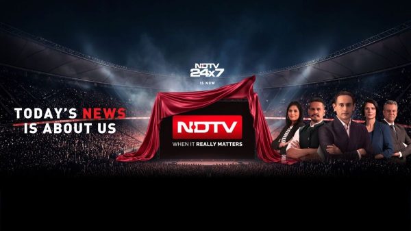 NDTV 24x7 illuminated studio stage with a red-draped screen revealing the NDTV logo and a team of anchors on the right, slogan: 'Today’s News Is About Us'.