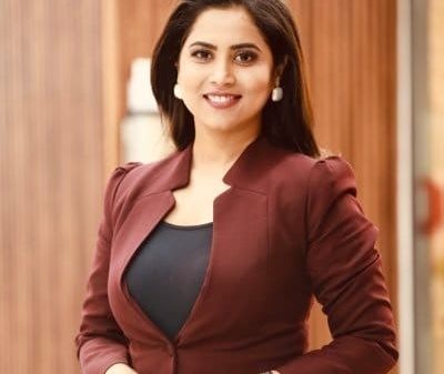Professional woman in a maroon blazer smiling at the camera, standing in a wood-paneled hallway.