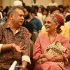 Two adults in a crowded hall share a smile while seated together, chatting at an event.