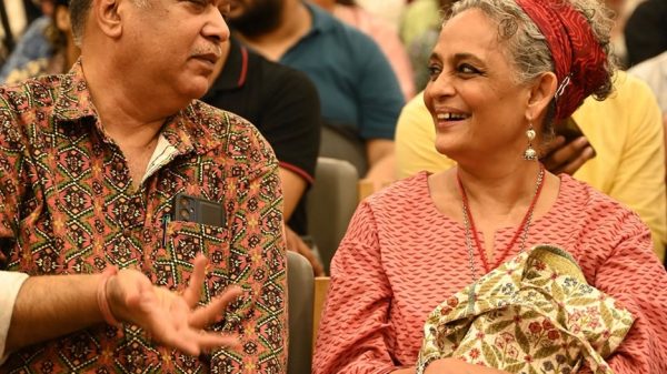 Two adults in a crowded hall share a smile while seated together, chatting at an event.