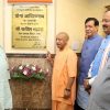 Group of Indian officials at a plaque unveiling ceremony with a saffron-robed man holding a chain and flower arrangement nearby