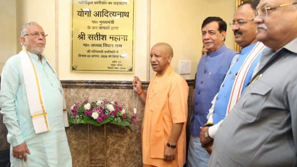 Group of Indian officials at a plaque unveiling ceremony with a saffron-robed man holding a chain and flower arrangement nearby