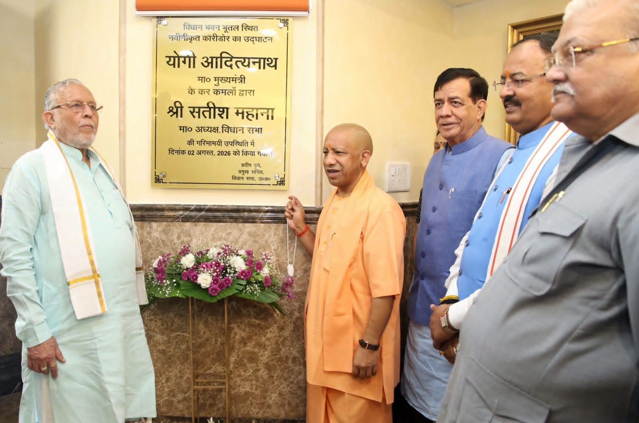 Group of Indian officials at a plaque unveiling ceremony with a saffron-robed man holding a chain and flower arrangement nearby