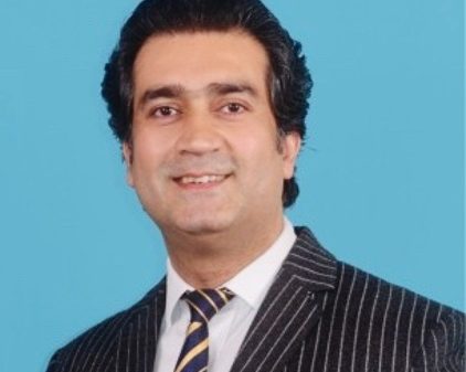 Professional portrait of a smiling man in a pinstripe suit against a light blue background.