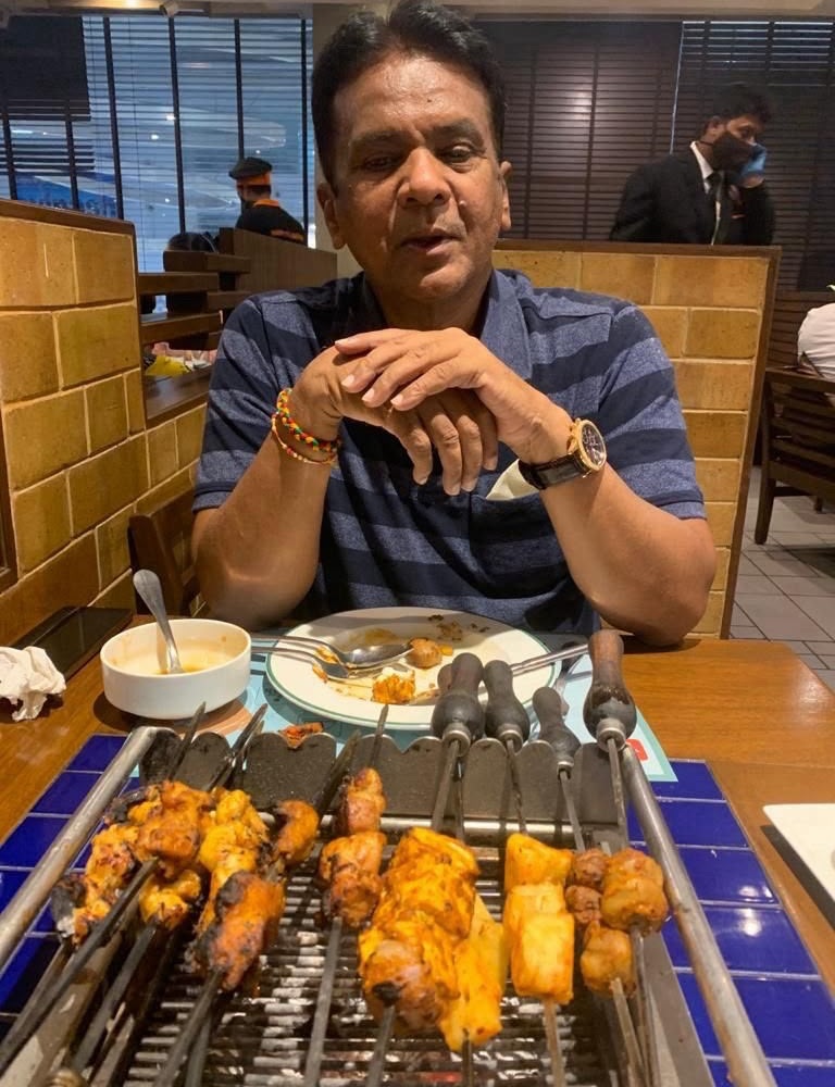 prem pathak | No. 1 Indian Media News Portal Man dining at a restaurant with a grill full of skewered kebabs in the foreground; he wears a blue striped polo, bracelets, and a watch.