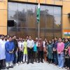 Group of people posing for a photo in front of a building, with an Indian flag raised on a tall pole behind them.