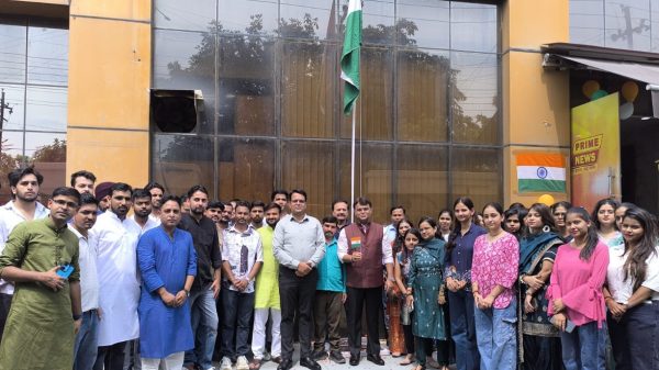 Group of people posing for a photo in front of a building, with an Indian flag raised on a tall pole behind them.