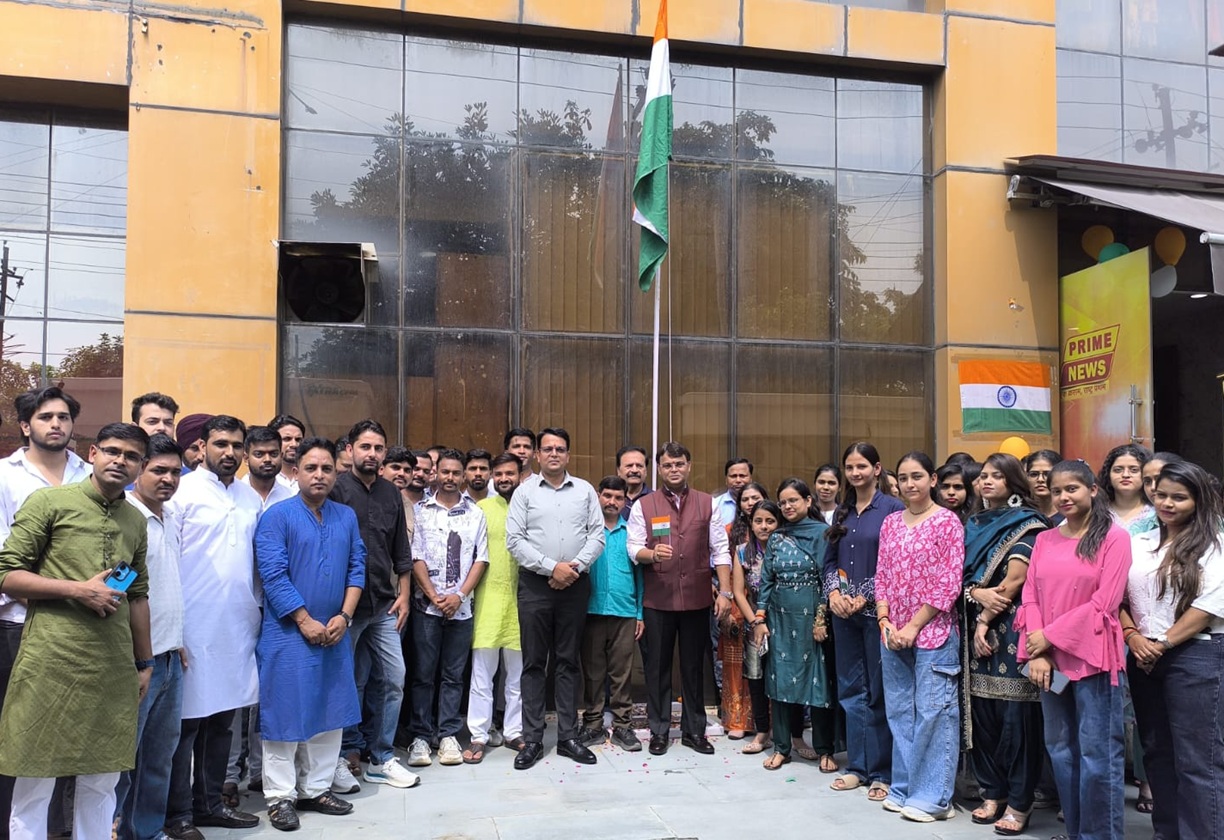 Group of people posing for a photo in front of a building, with an Indian flag raised on a tall pole behind them.