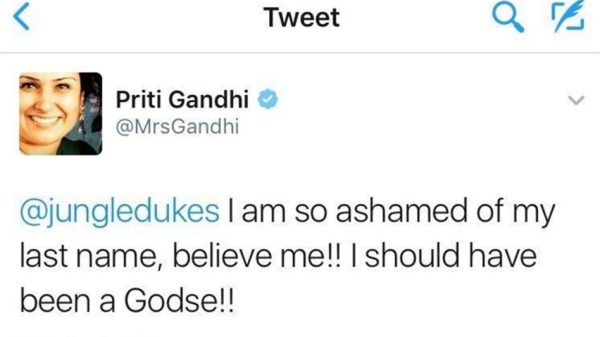 Screenshot of a Twitter post: profile picture of a smiling woman, blue verified badge, text reads "@jungledukes I am so ashamed of my last name, believe me!! I should have been a Godse!!"