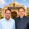 Two men pose in front of the Uttar Pradesh Legislative Assembly building, with a domed facade, ornate arches, and the Indian flag overhead.