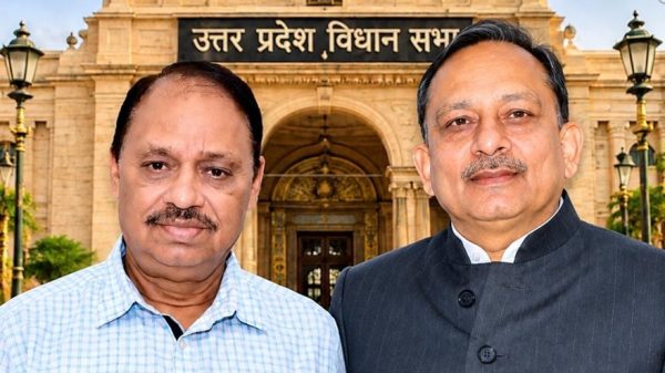 Two men pose in front of the Uttar Pradesh Legislative Assembly building, with a domed facade, ornate arches, and the Indian flag overhead.
