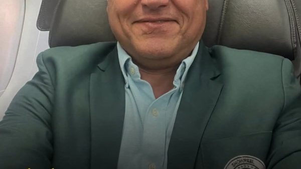Portrait of a bald man in a green blazer on an airplane seat, overlaid with a quote about Gujaratis and money attributed to Sabeer Bhatia.