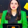 Female news anchor in a bright green blazer delivering a broadcast from a studio backdrop.