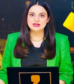 Female news anchor in a bright green blazer delivering a broadcast from a studio backdrop.