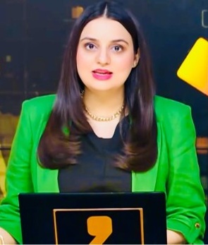 Female news anchor in a bright green blazer delivering a broadcast from a studio backdrop.