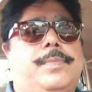 Close-up of a man with a thick mustache wearing dark sunglasses, looking slightly to the side.