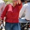 Woman in a red polka-dotted blouse and sunglasses smiles and flashes a peace sign toward the camera outdoors.