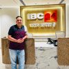 Man standing at a marble reception desk in front of a lit IBC 24 sign with a yellow backdrop and Arabic-style lettering above