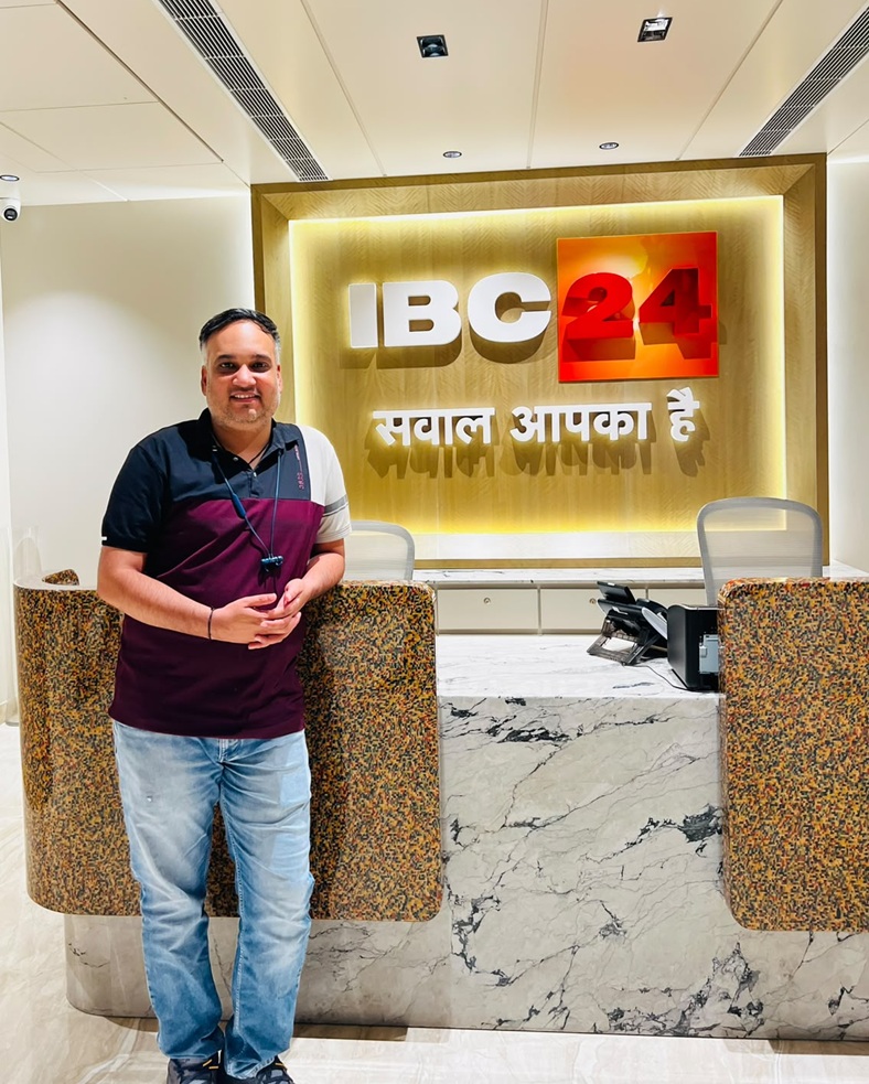 Man standing at a marble reception desk in front of a lit IBC 24 sign with a yellow backdrop and Arabic-style lettering above