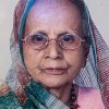 Portrait of an elderly woman wearing a multicolor headscarf and round glasses, looking at the camera.