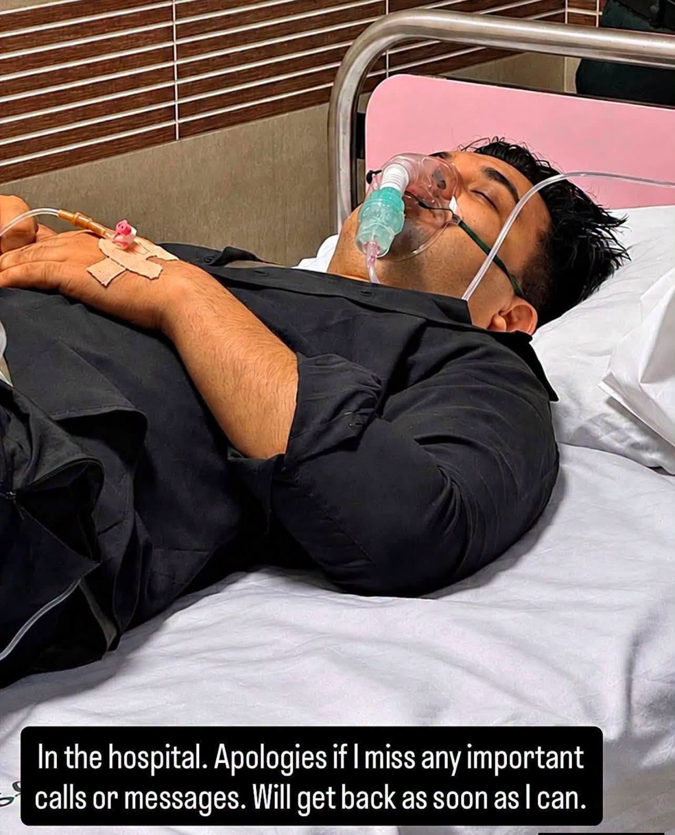 Man lying in hospital bed with an oxygen mask and IV tubing, resting with eyes closed.