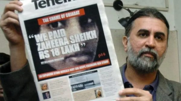 Man with gray beard holds a Tehelka newspaper showing a large central image and bold headline front page.