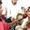 Female reporter in a pink top interviews a bearded man in traditional attire; hands folded in prayer as he speaks.