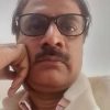 Man with rectangular glasses and mustache resting his chin on his hand, looking at the camera in a close-up shot.