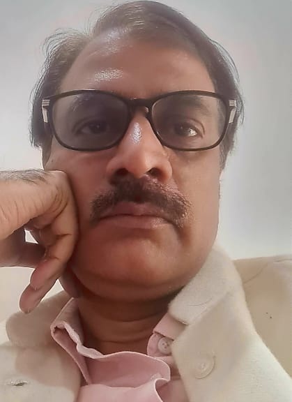 Man with rectangular glasses and mustache resting his chin on his hand, looking at the camera in a close-up shot.