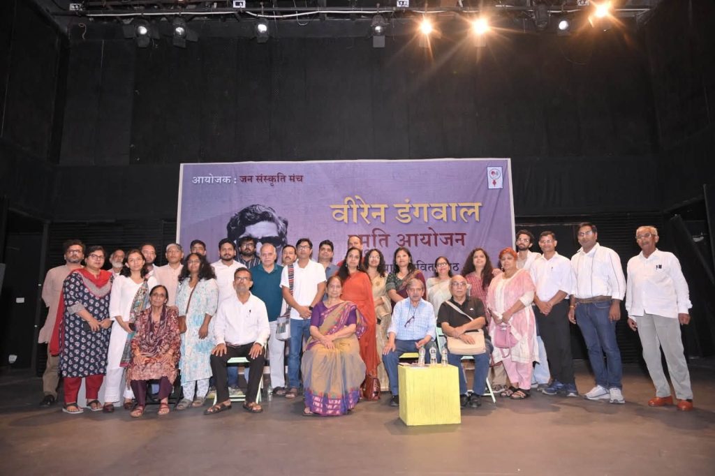 viren ji_4 | No. 1 Indian Media News Portal Group of men and women posing on a stage in front of a purple banner for a cultural event photo. Behind them, the banner displays Hindi text and a portrait image.