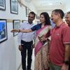 Woman in a pink sari points at a framed picture on a gallery wall while a group of people looks on and smiles has a casual gallery setting.