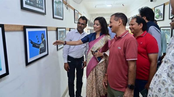 Woman in a pink sari points at a framed picture on a gallery wall while a group of people looks on and smiles has a casual gallery setting.