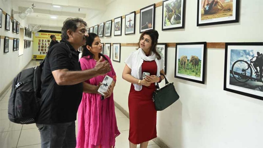 world photography_1 | No. 1 Indian Media News Portal Three people in a hallway gallery viewing framed photographs on the wall, with the man gesturing as he talks.