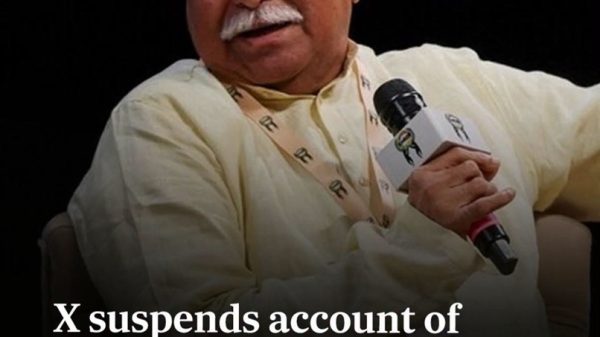 An older man with white hair and mustache sits on stage, holding a microphone, wearing a pale yellow shirt; a bold headline overlays the image about X suspending the RSS chief Mohan Bhagwat’s New York event organizers.