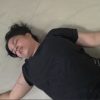 Woman in a black shirt lying on a light tile floor, eyes closed, arms spread, holding a pink object in her right hand.
