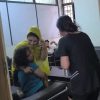 Woman in a yellow hijab comforts a crying child who is being hugged by another woman in a clinic waiting room as a staff member approaches.