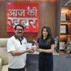 Two people exchange a red mug in a showroom, with a wooden wall and award shelf in the background.