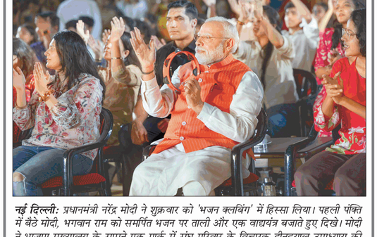 Center-stage is an elderly man with a white beard wearing an orange vest and white kurta, clapping while holding a red cap, surrounded by a cheering audience at a public event.