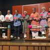 Diverse group of people on stage holding pink-and-gray books during a book launch event.