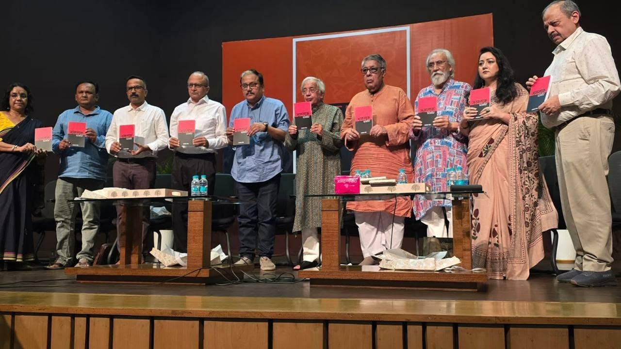 Diverse group of people on stage holding pink-and-gray books during a book launch event.