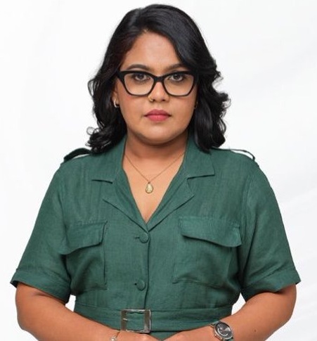 Portrait of a woman with dark hair and glasses, wearing a green short-sleeve button-down dress with a belt, posing against a white background.