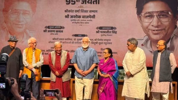 Eight people stand on a stage for a commemorative event, with a large banner announcing '95th Jayanti' in Hindi behind them.