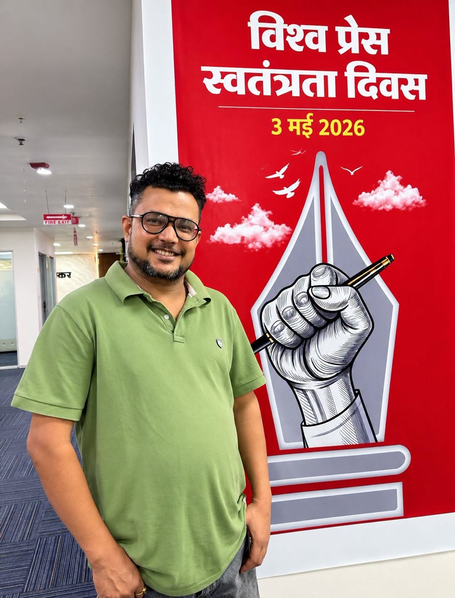 Man in a green polo shirt smiles beside a large red banner that reads 'World Press Freedom Day' with '3 May 2026', featuring a fist gripping a pencil.