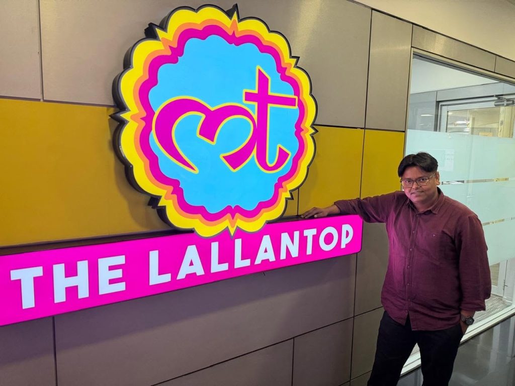 avinash rai | No. 1 Indian Media News Portal Man in a maroon shirt leaning on a neon pink sign that reads THE LALLANTOP next to a bright, circular logo on a panelled wall.