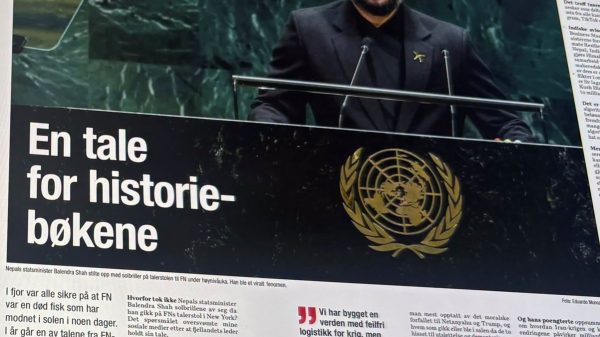 Man in a black suit and hat speaks at a United Nations podium with a large black banner reading 'En tale for historie-bøkene' in the foreground (news photo).