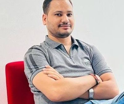 Man with short beard sits in a red chair with arms crossed, wearing a gray polo shirt.